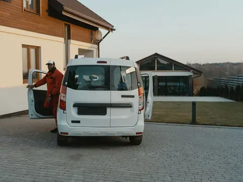 A white work van in a paved yard with its driver stepping out