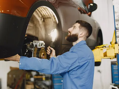 A smiling technician checking the wheel arch of a car on a lift